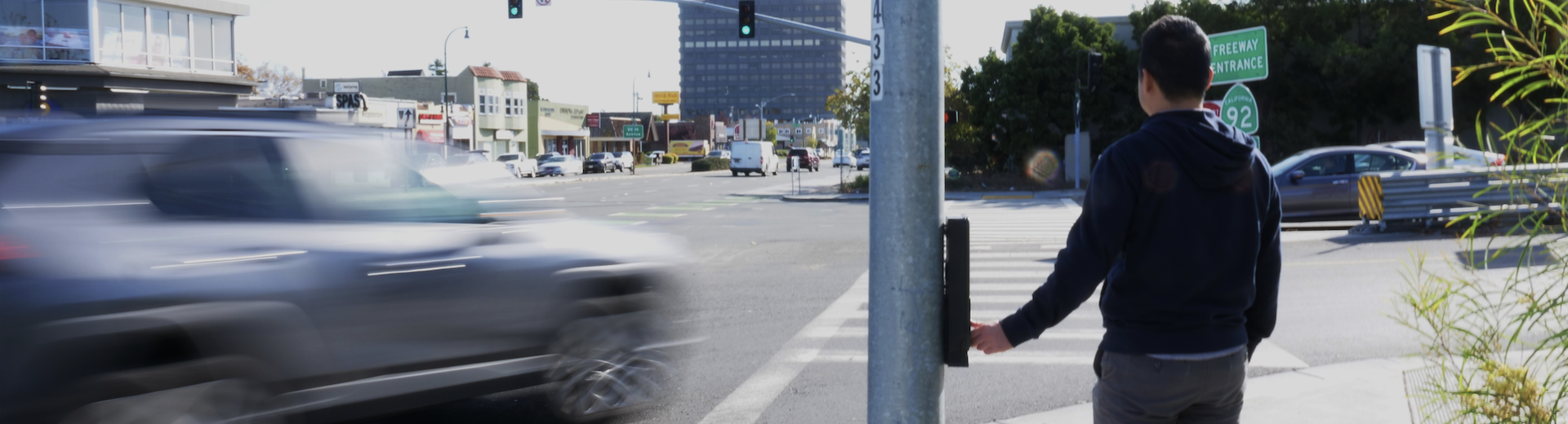 A pedestrian waits for traffic along a busy stretch of El Camino Real in San Mateo