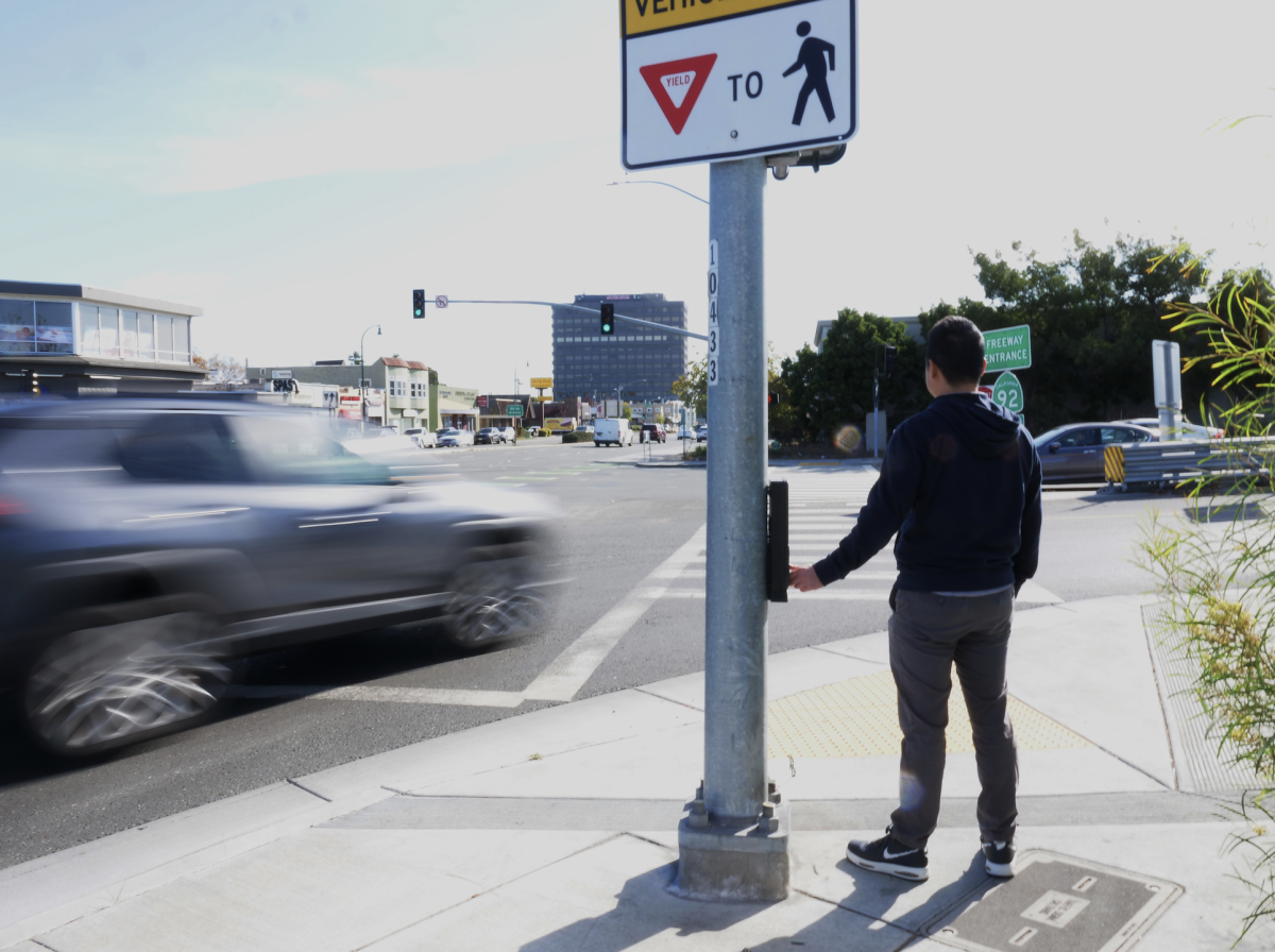 A pedestrian waits for traffic along a busy stretch of El Camino Real in San Mateo